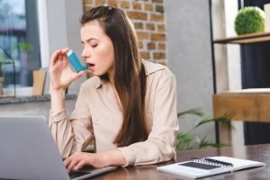 young businesswoman with asthma using inhaler in office young businesswoman with asthma using inhaler in office
